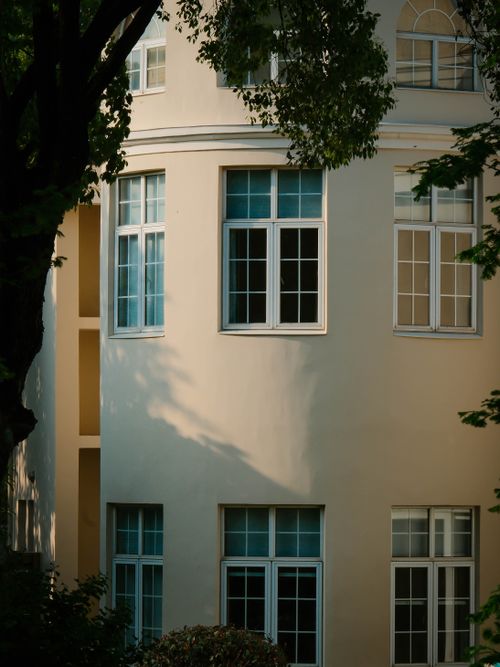 Free A beautifully lit curved building facade with trees and windows casting shadows in warm evening light. Stock Photo