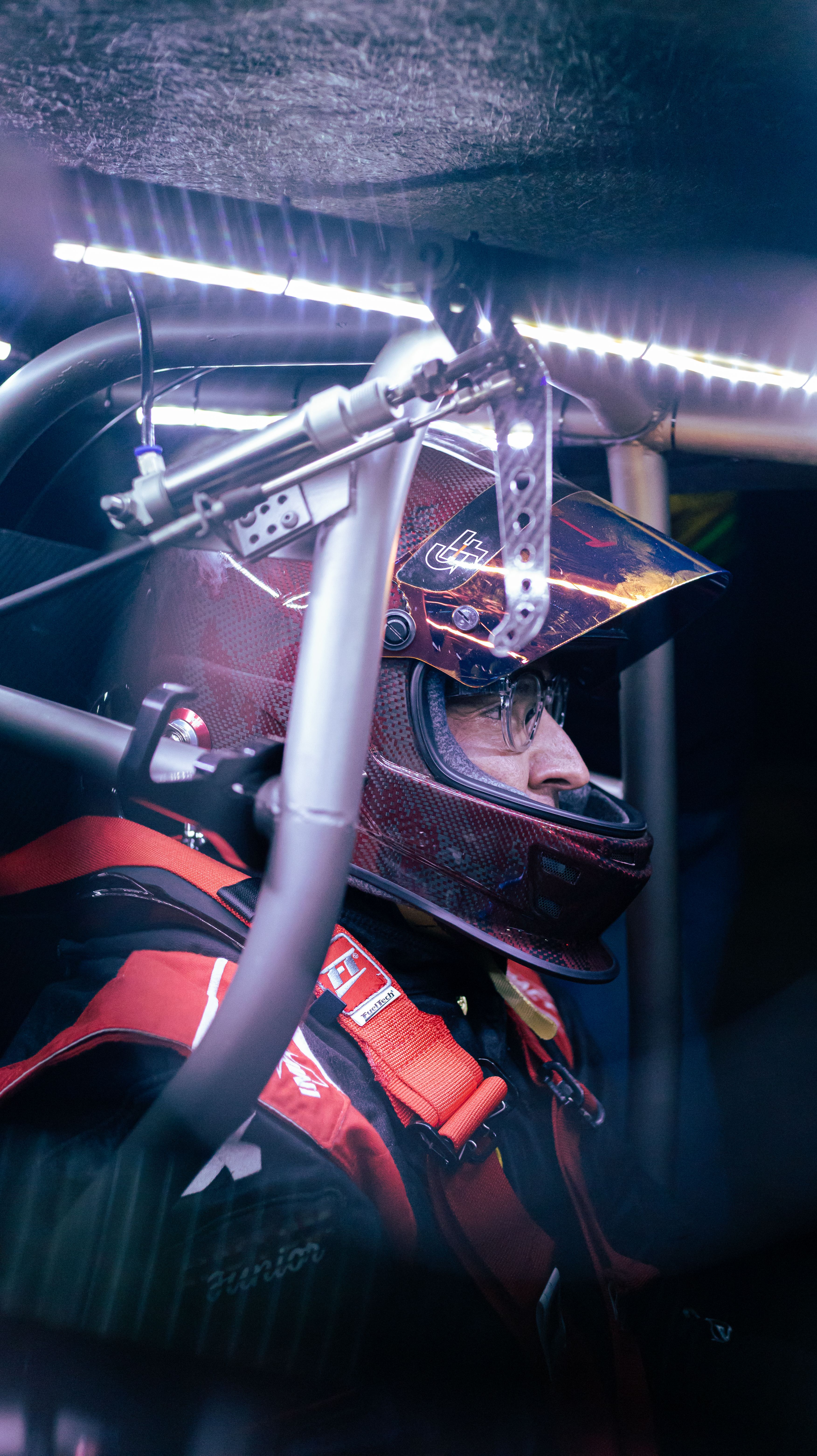 Side profile of a race car driver inside a vehicle with helmet and safety gear on.