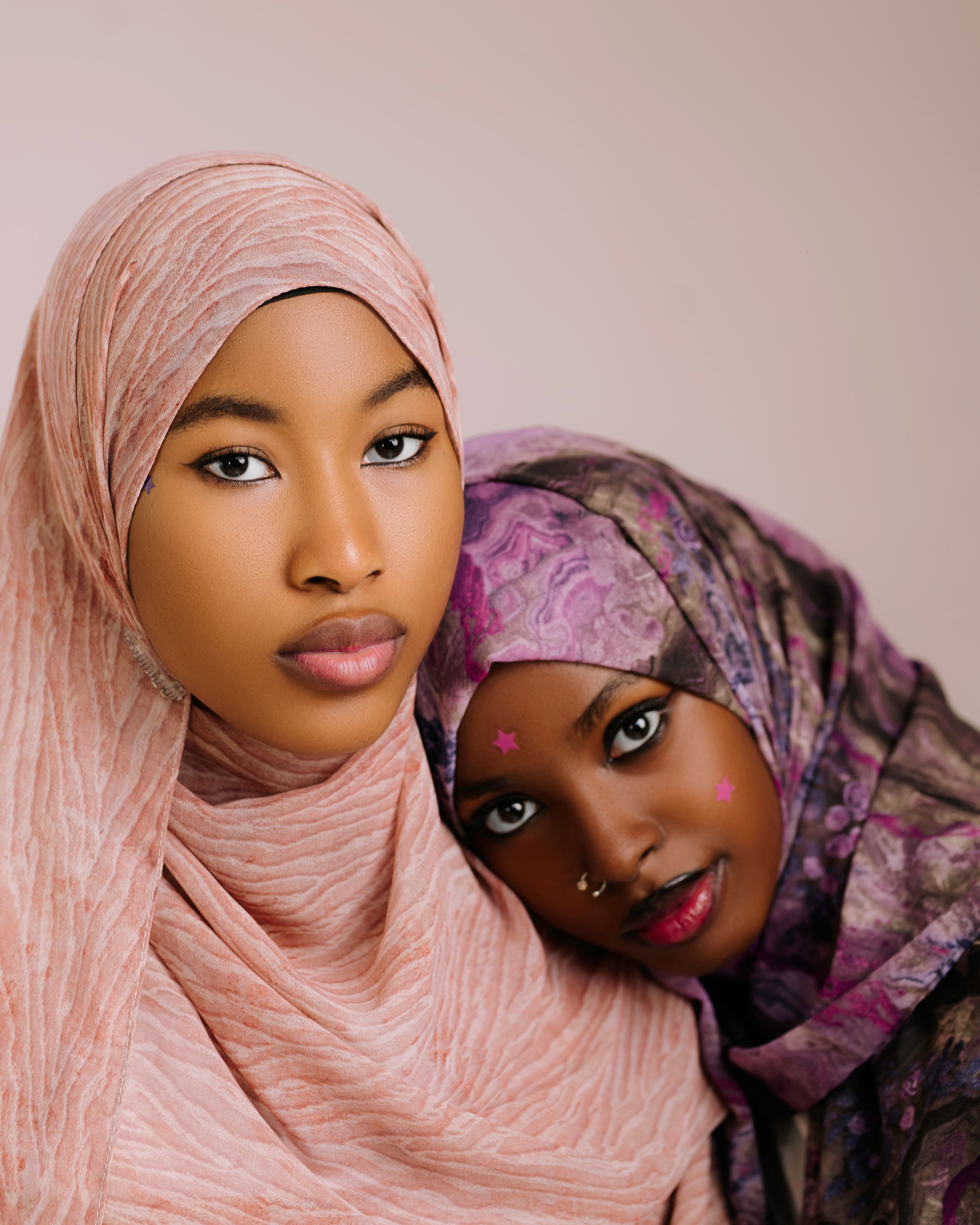 Close-up portrait of two stylish women wearing beautifully patterned hijabs with expressive makeup.