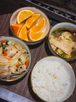Delicious homemade chicken soup, rice, and fresh orange slices served in elegant bowls.