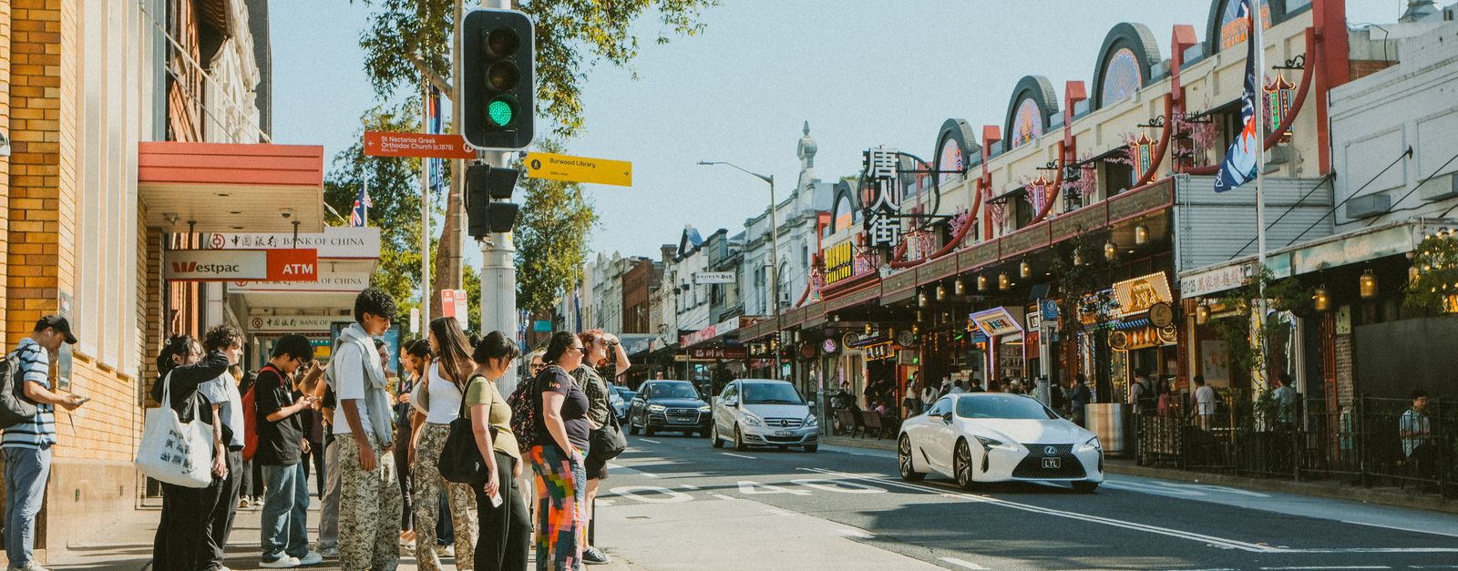 A bustling urban street with diverse pedestrians waiting at a crosswalk.