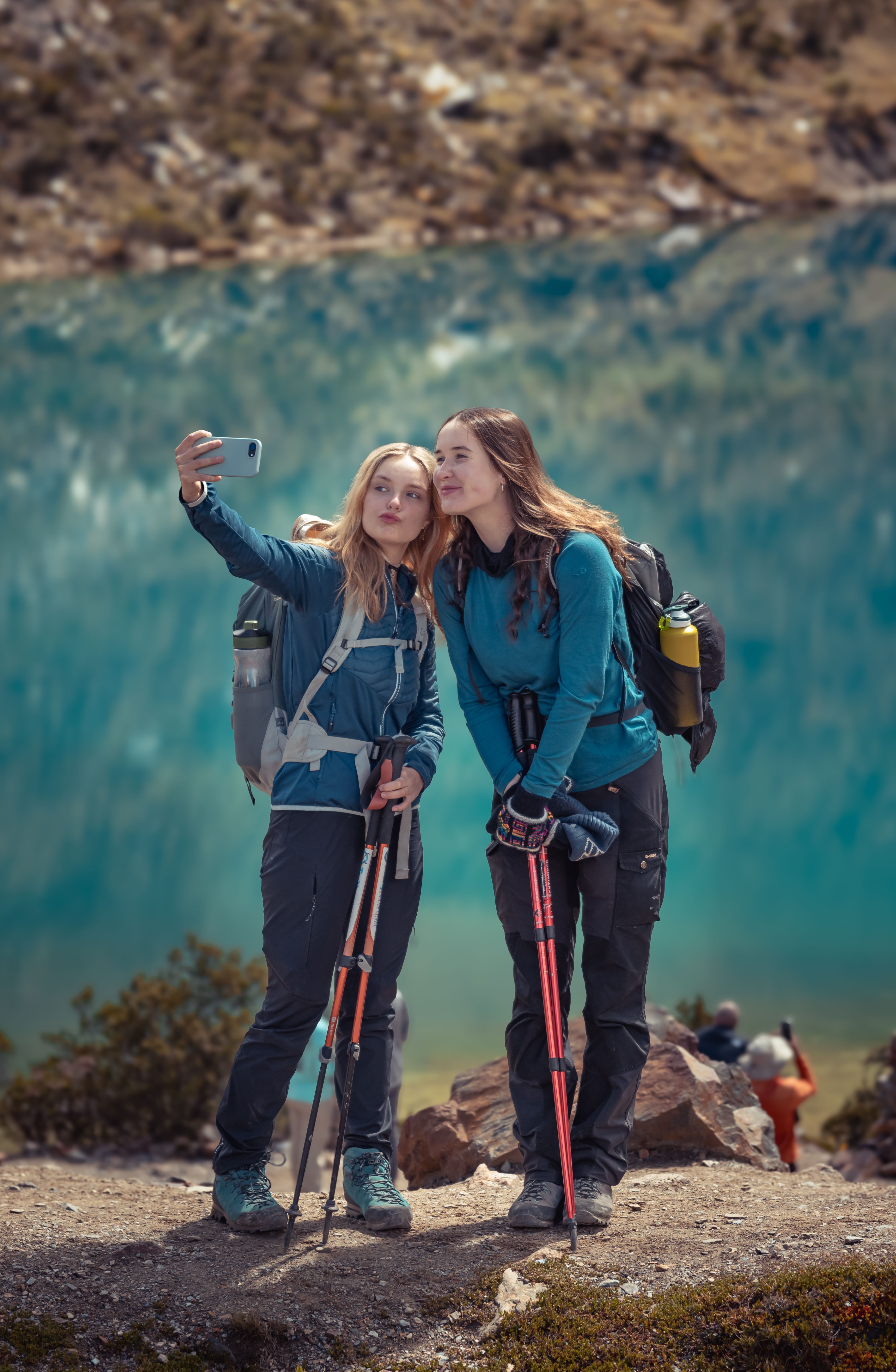 Two women enjoying a hike near a scenic mountain lake, capturing memories with a selfie.