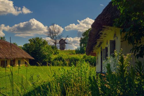Free Picturesque rural landscape with cottages and a traditional windmill under a blue sky. Stock Photo