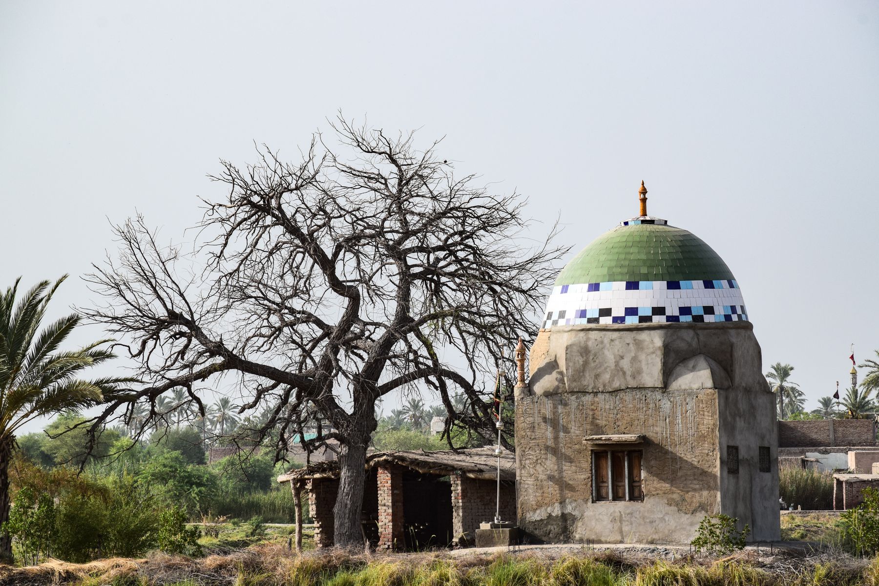 A historic small mosque with a green dome and intricate patterns in rural Kandiāro, Sindh, Pakistan.
