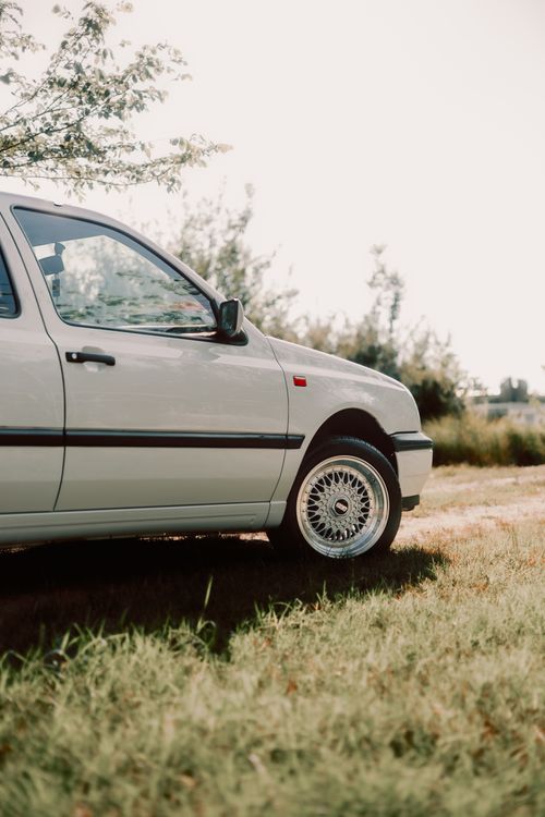 Free A classic white car parked on grass with a serene outdoor backdrop, captured during daytime. Stock Photo