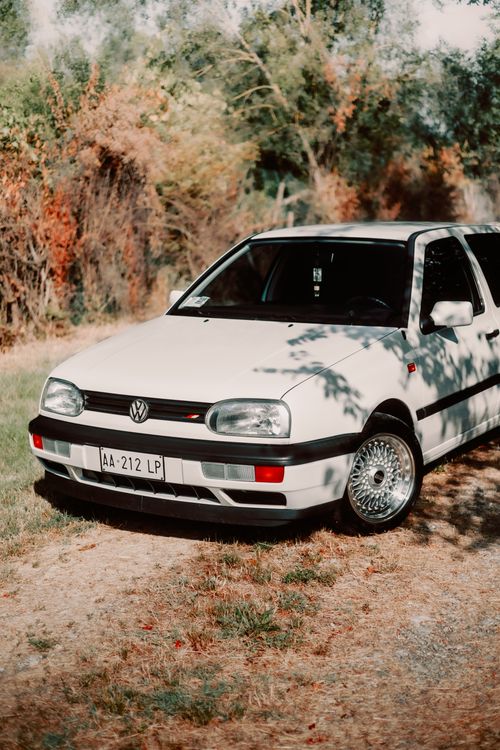 Free A classic white Volkswagen car parked on a grassy field surrounded by nature in an outdoor setting. Stock Photo