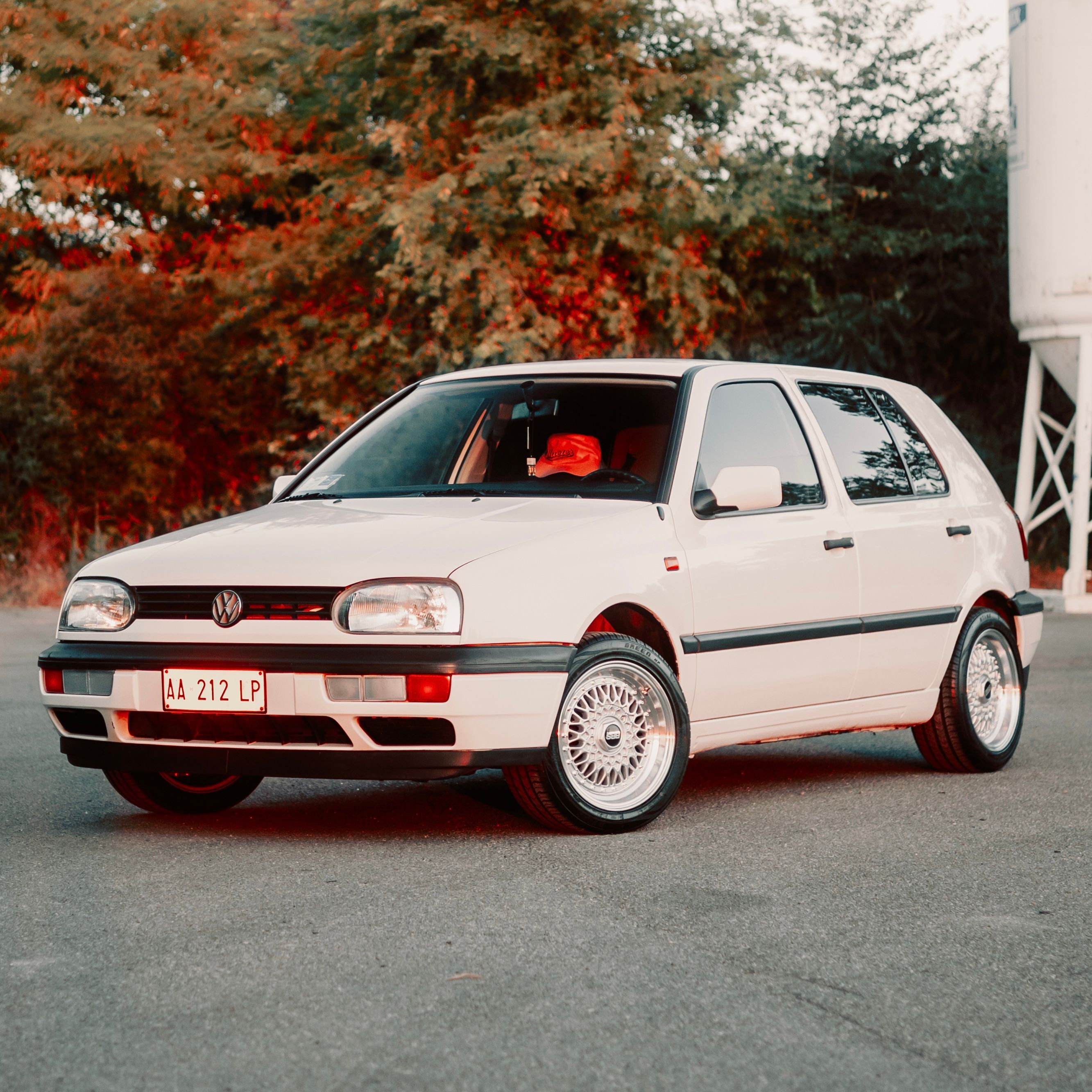 Vintage white Volkswagen Golf Mk3 parked outdoors with autumn backdrop.