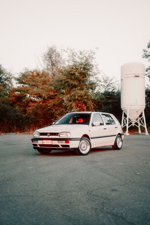 Free Classic white car parked in an urban area with a water tower and trees in the background. Stock Photo