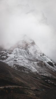 A dramatic view of a snow-capped mountain peak shrouded in mist during autumn.