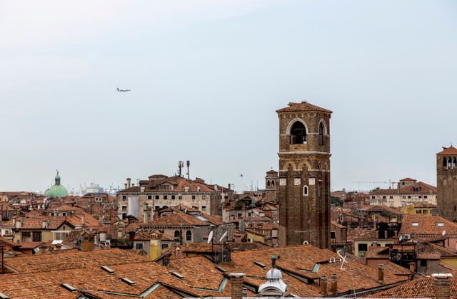Scenic view of Venice rooftops featuring a historic bell tower and distant airplane in the sky. — arriving in Venezia