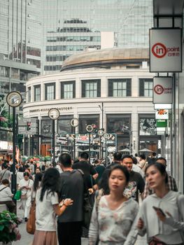 Urban street scene with diverse crowd near a contemporary building in a bustling city.