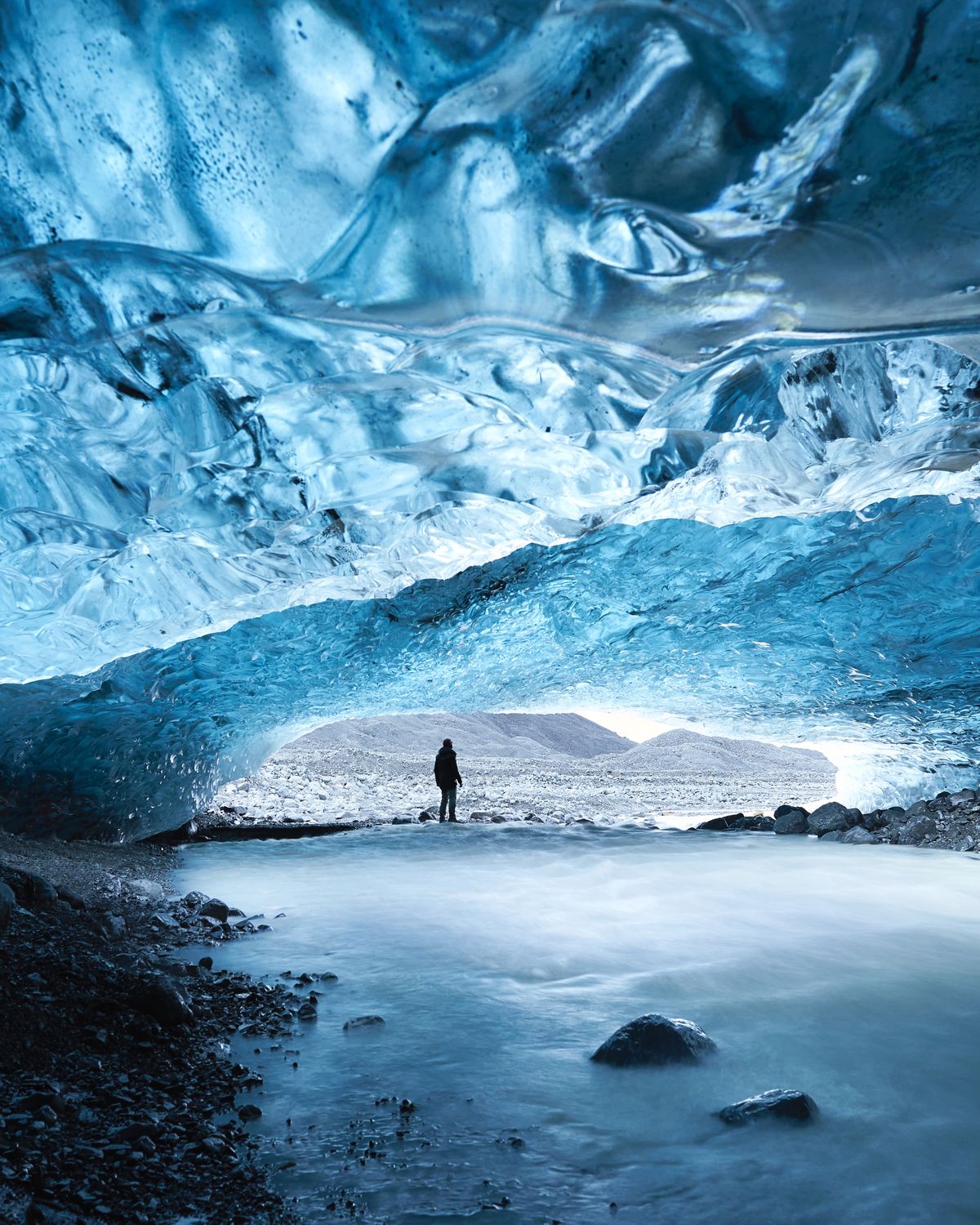 The inside of the Icehotel in Jukkasjärvi, Sweden — blue-lit ice walls and an arched ice ceiling over a bed of reindeer skins