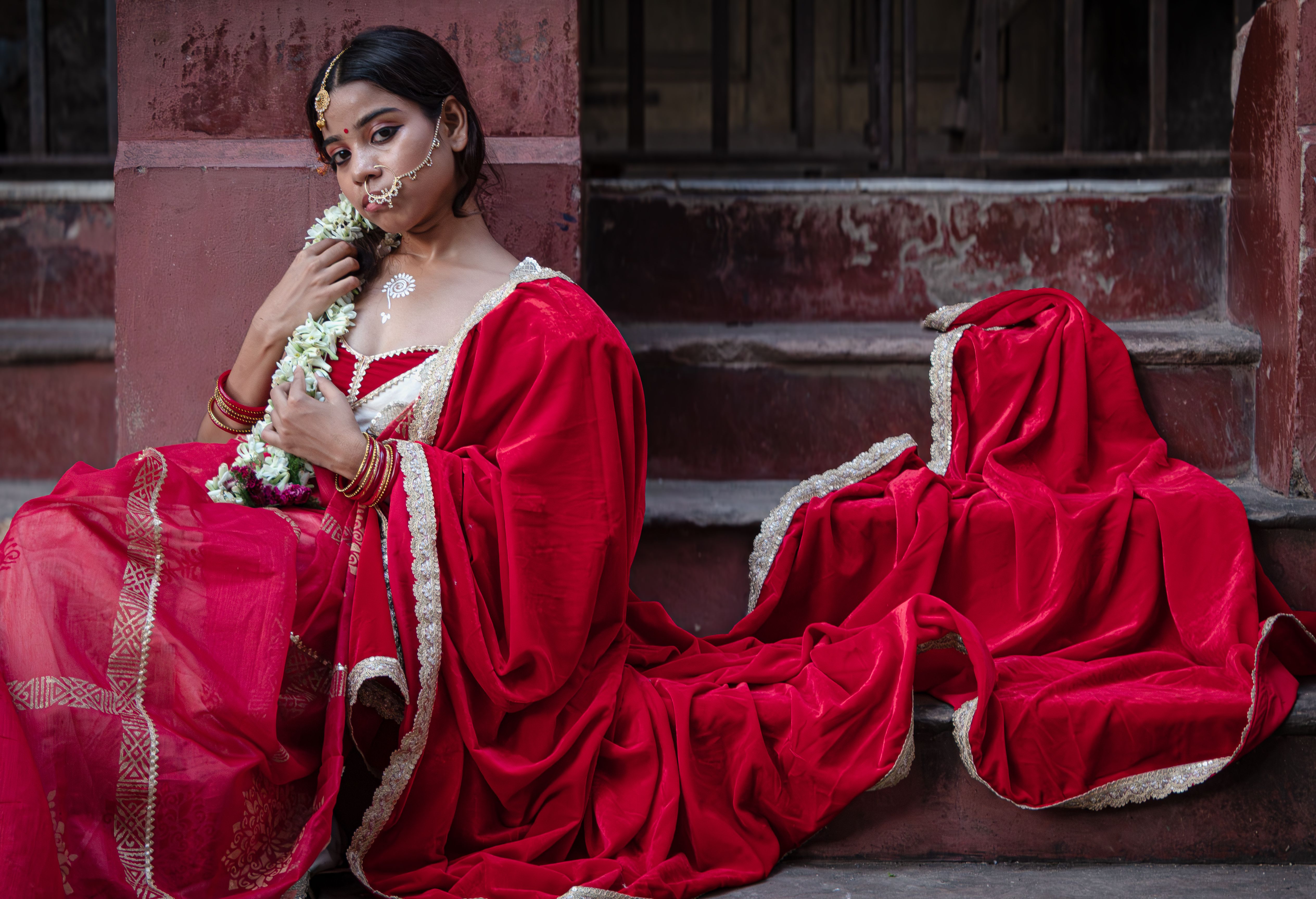 A woman in a vibrant red sari, adorned with traditional Indian jewelry, seated outdoors.