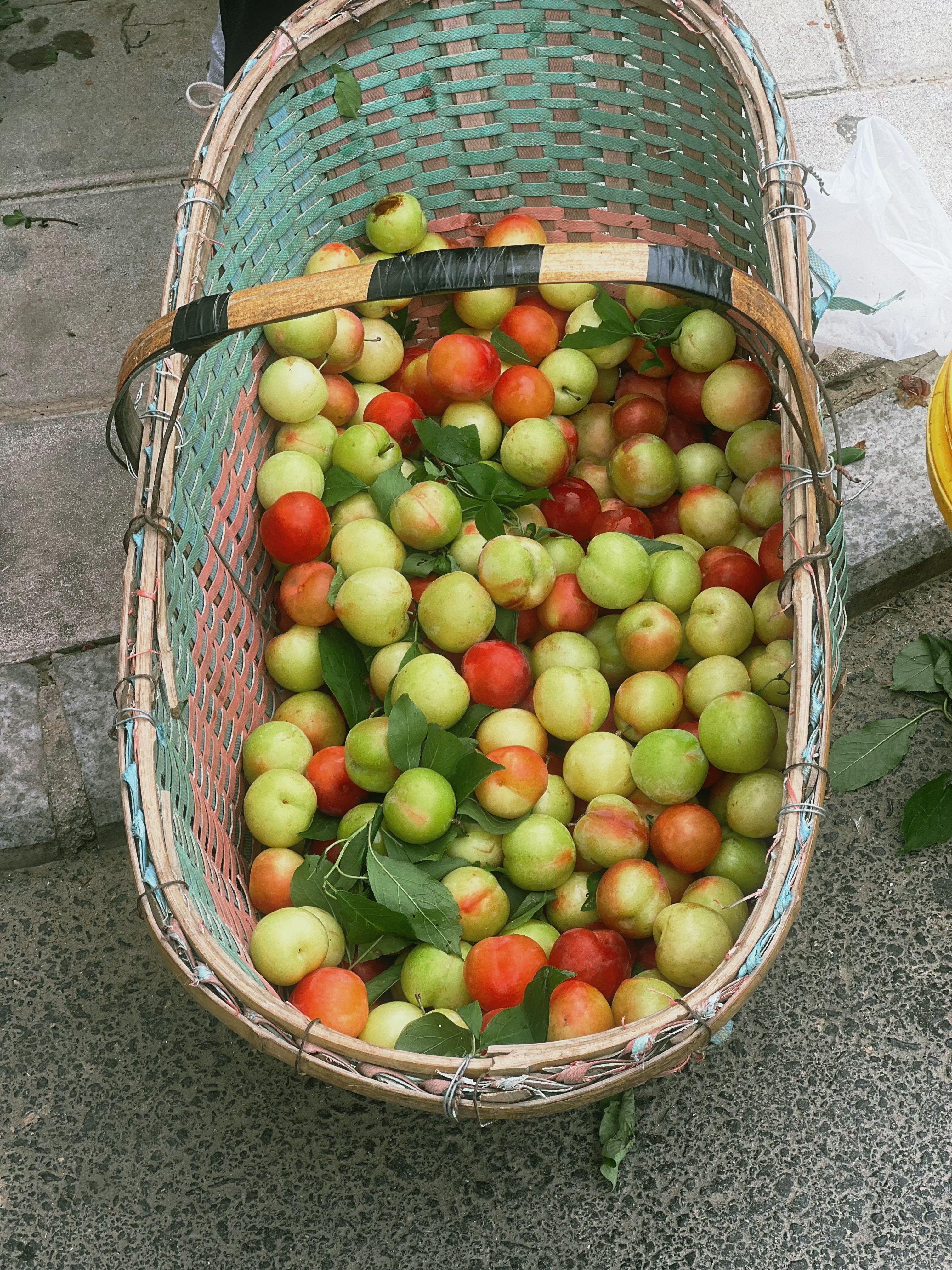 Colorful jujubes in a wicker basket displayed outdoors on a stone surface.