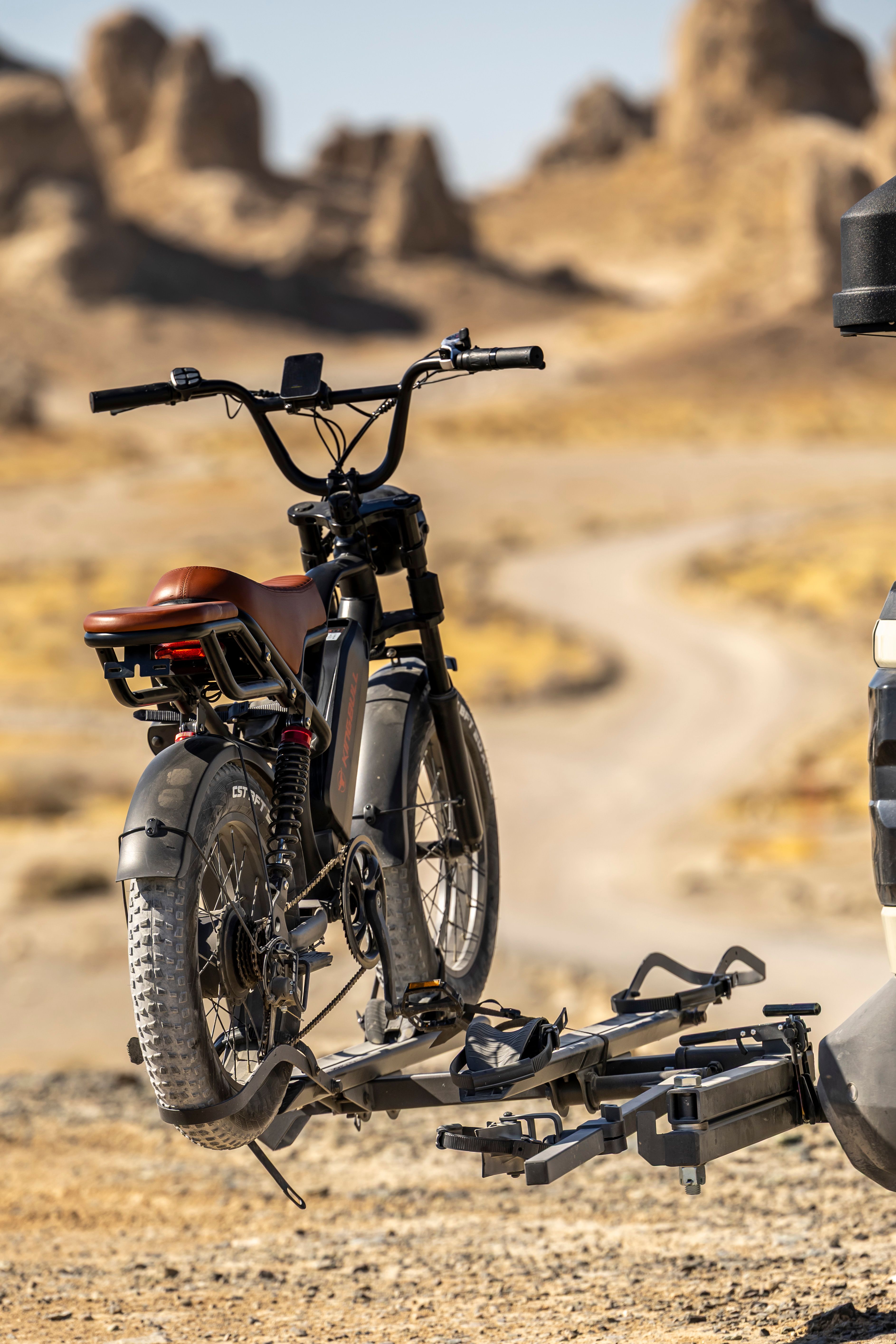 Electric bike secured on a vehicle rack in a desert landscape under a clear sky.