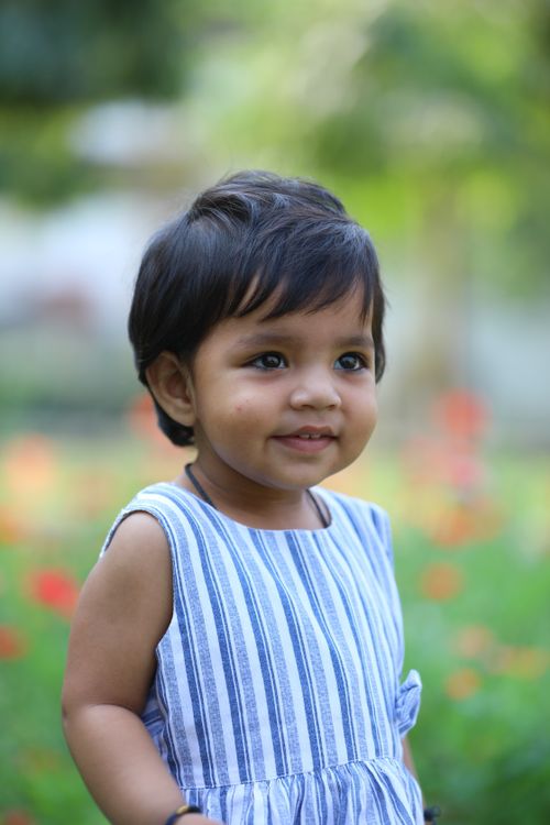 Free Charming portrait of a baby girl in a striped dress outdoors with flowers. Stock Photo