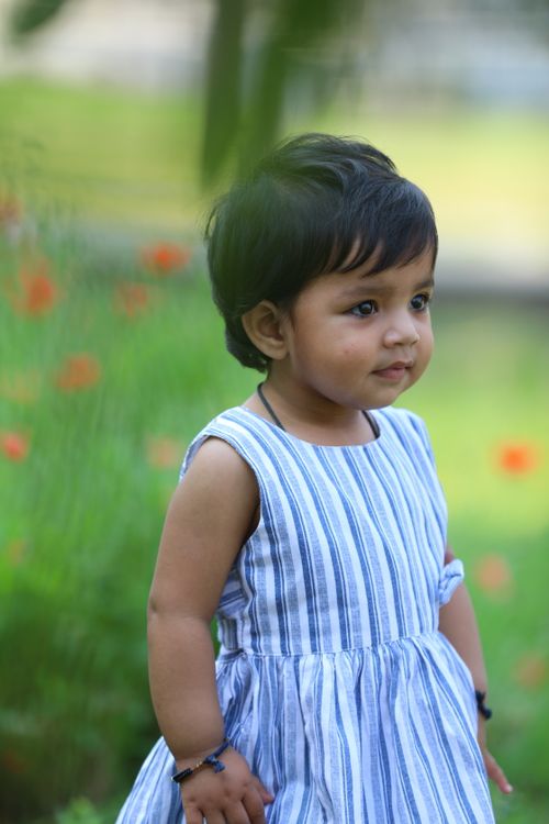 Free Charming portrait of a toddler in a blue-striped dress, enjoying a sunny day outdoors. Stock Photo