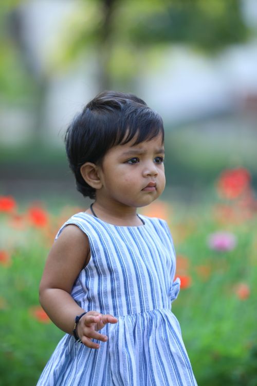 Free Charming portrait of a toddler in a striped dress enjoying a sunny day in the garden. Stock Photo