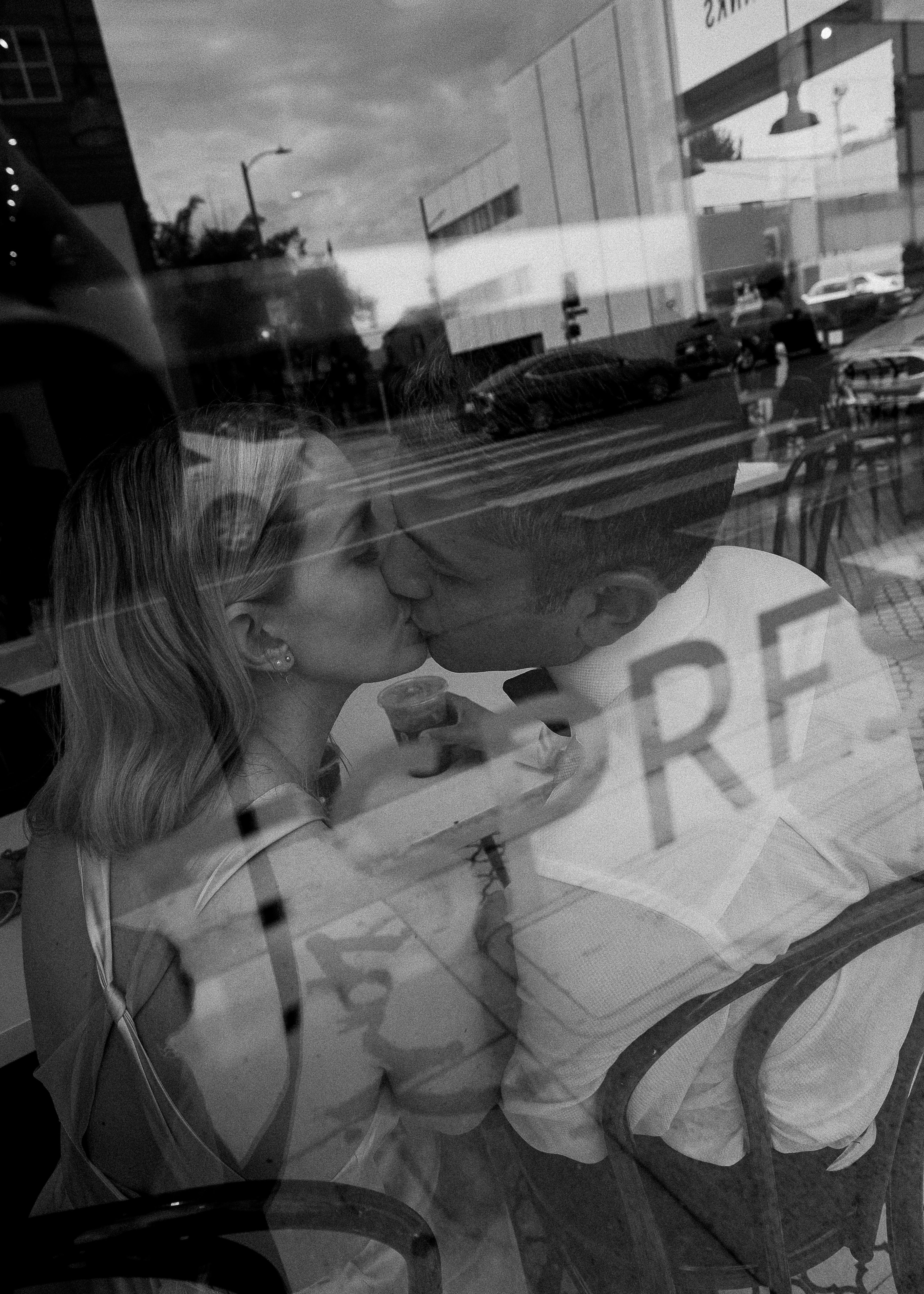 A couple shares a romantic kiss in a Los Angeles cafe, captured through the window.