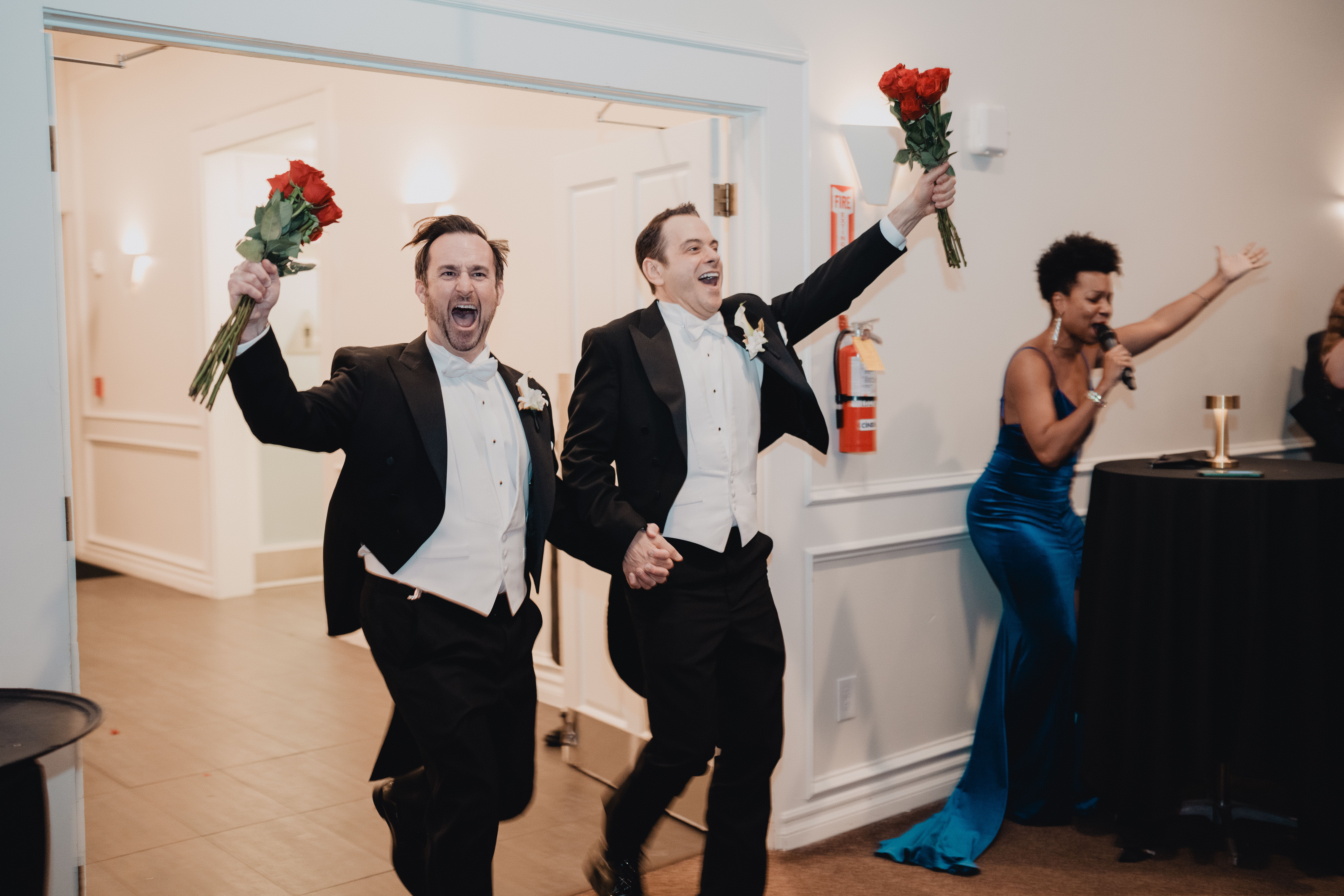 Two grooms celebrate their wedding entrance with roses, captured with vibrant emotion in Los Angeles.
