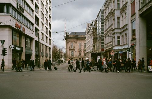 Free Side view of unrecognizable pedestrians crossing road near old residential buildings in city on overcast day Stock Photo