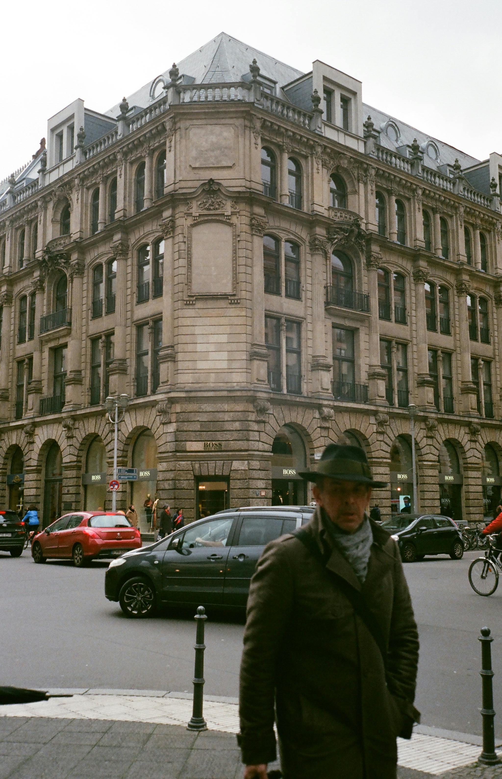 man in green jacket wearing hat standing on the street near cars and building