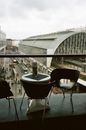 View from contemporary cafeteria with cozy chairs and small round table near fence in front of construction exterior and people walking on street in town