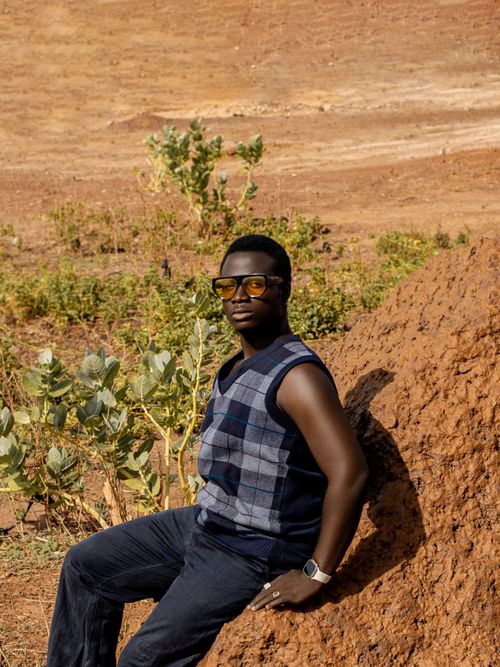 Free Individual in desert landscape wearing sunglasses, leaning on rock. Stock Photo