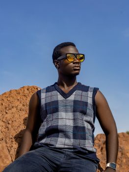 Young man wearing sunglasses and plaid shirt outdoors against a clear blue sky.