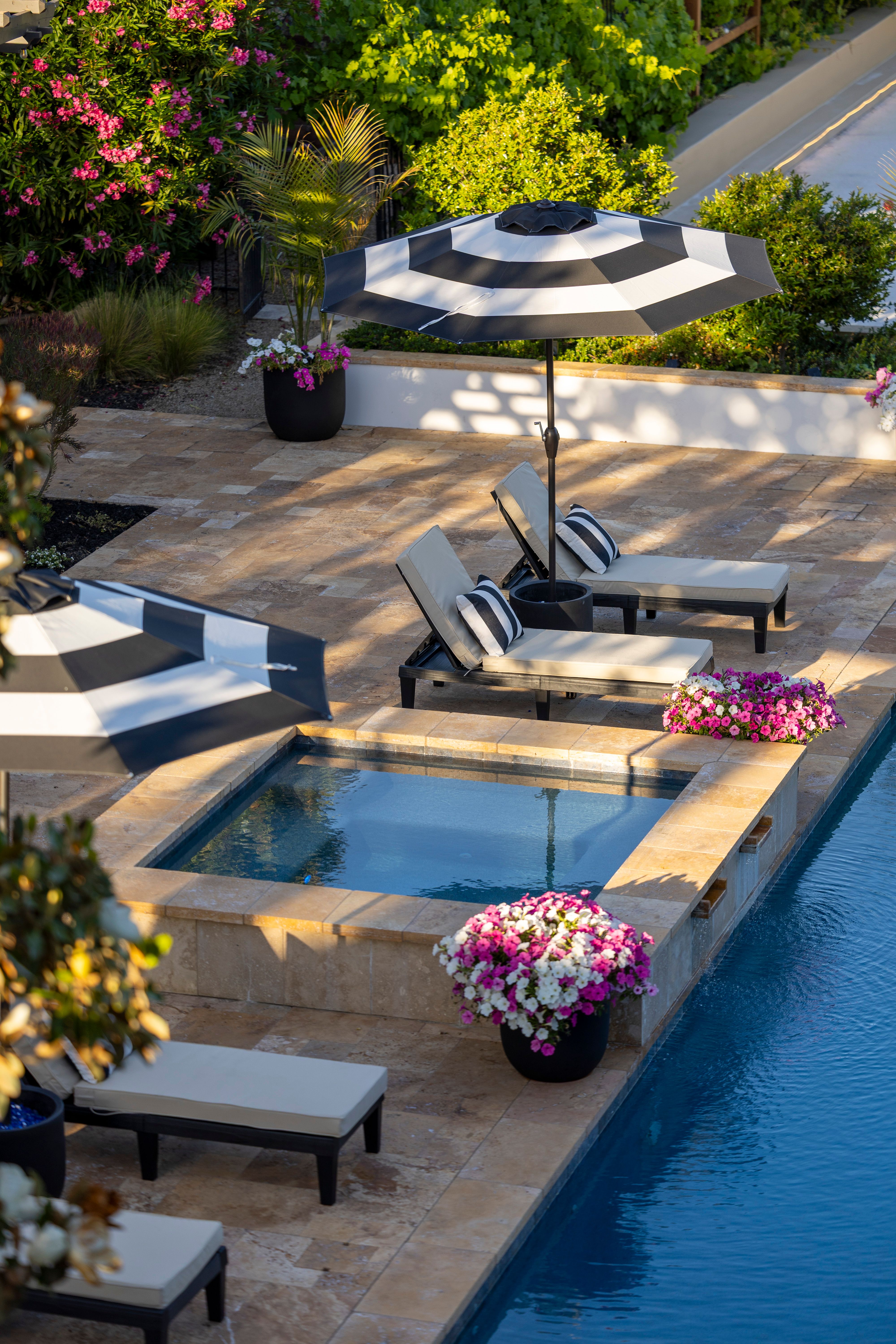 Elegant poolside scene featuring loungers and striped umbrellas in a serene garden setting.