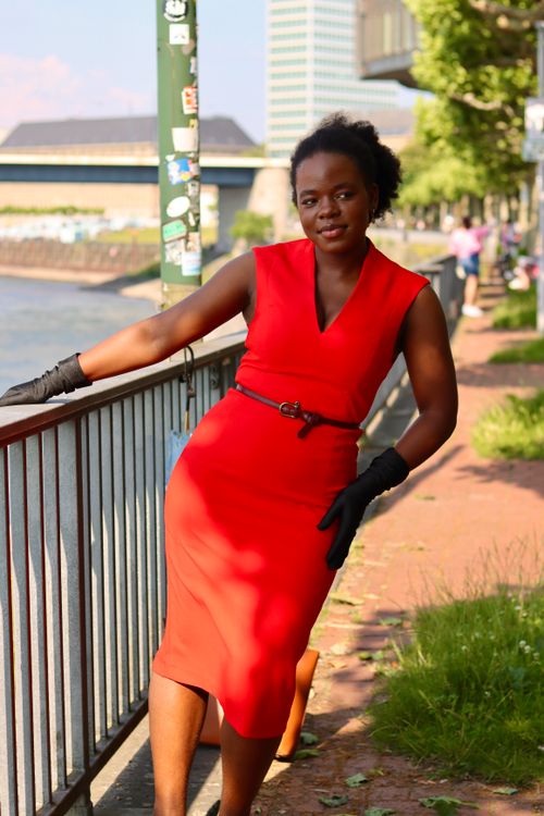 Free Fashionable woman in red dress leans on railing by waterfront in Düsseldorf, Germany. Stock Photo