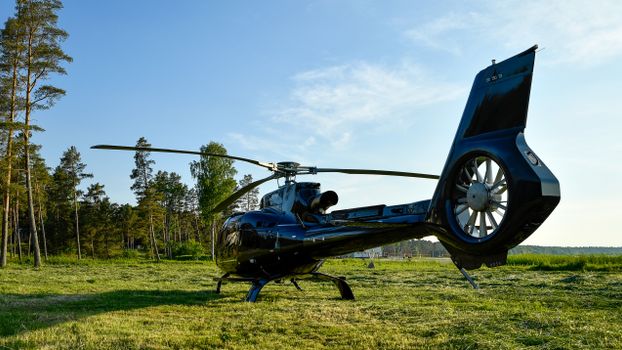 Black luxury helicopter on grassy field in Võsu, Estonia on a sunny day.