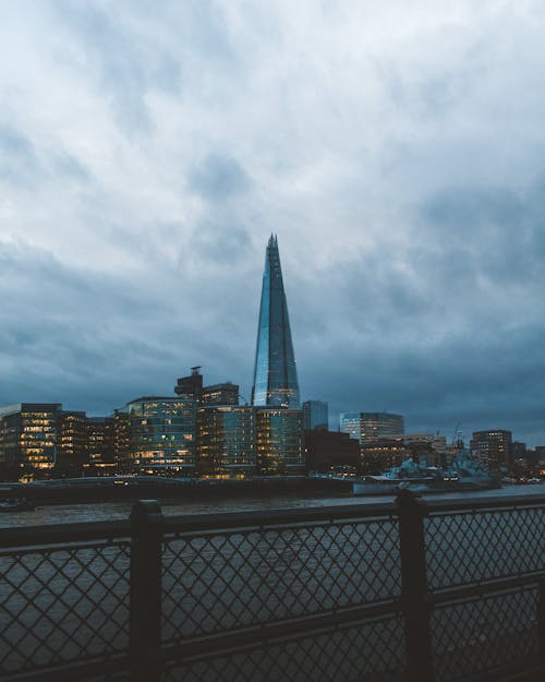 Modern buildings located near river on city street in evening time in cloudy weather