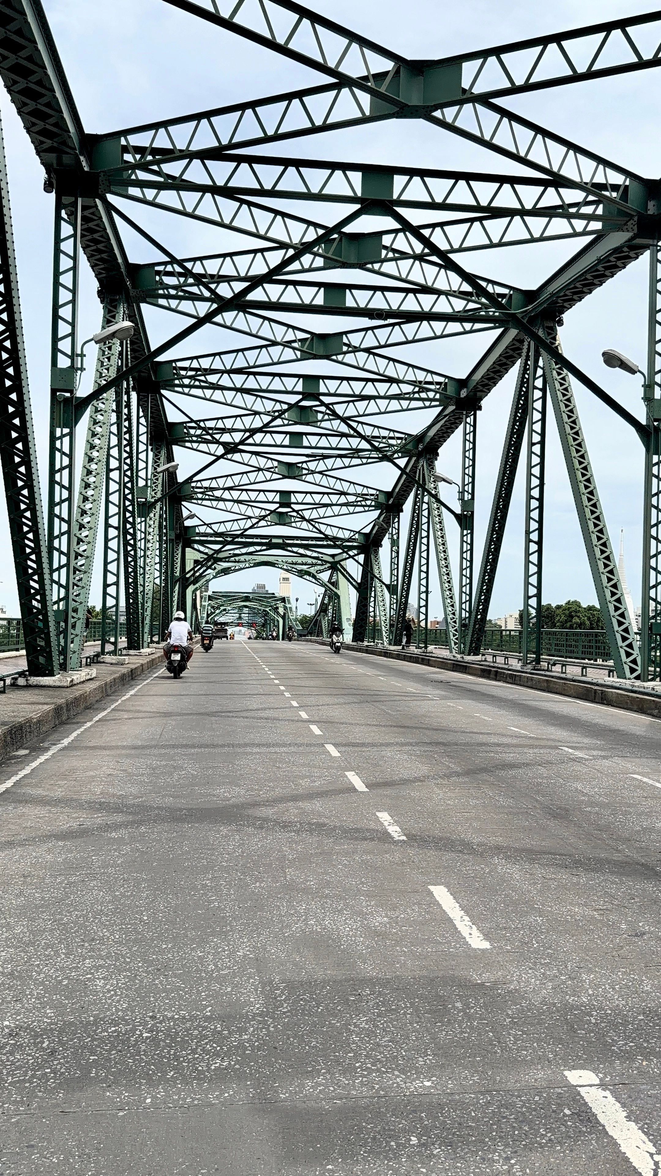 Steel truss bridge spanning a river with few motorists crossing on a clear day.