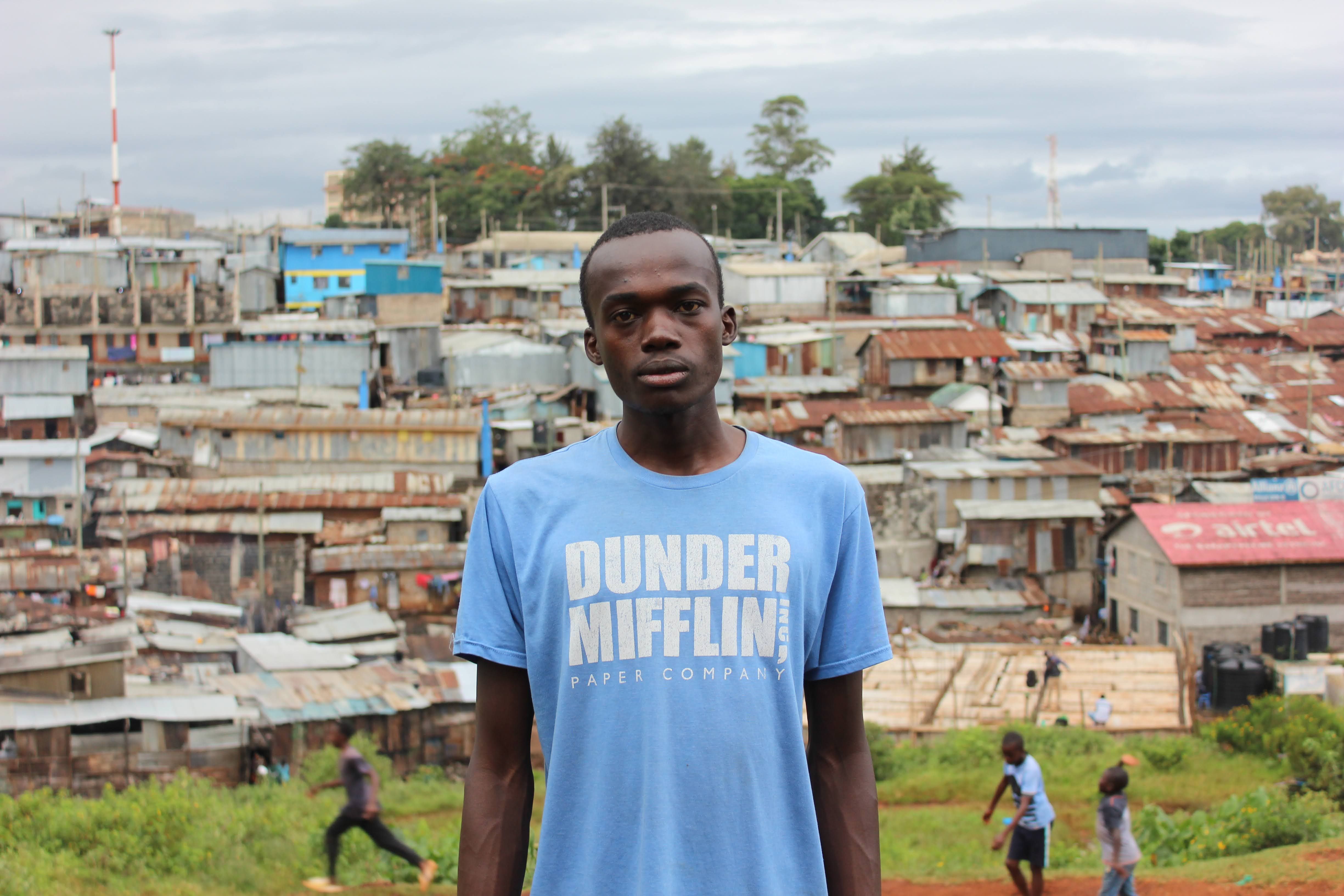 A young man stands in front of Nairobi's Kibera slum, showcasing urban life and community spirit.