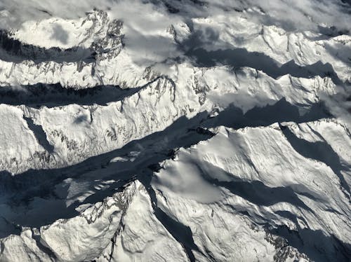 Drone view of rough mountainous terrain covered with snow among clouds in winter time