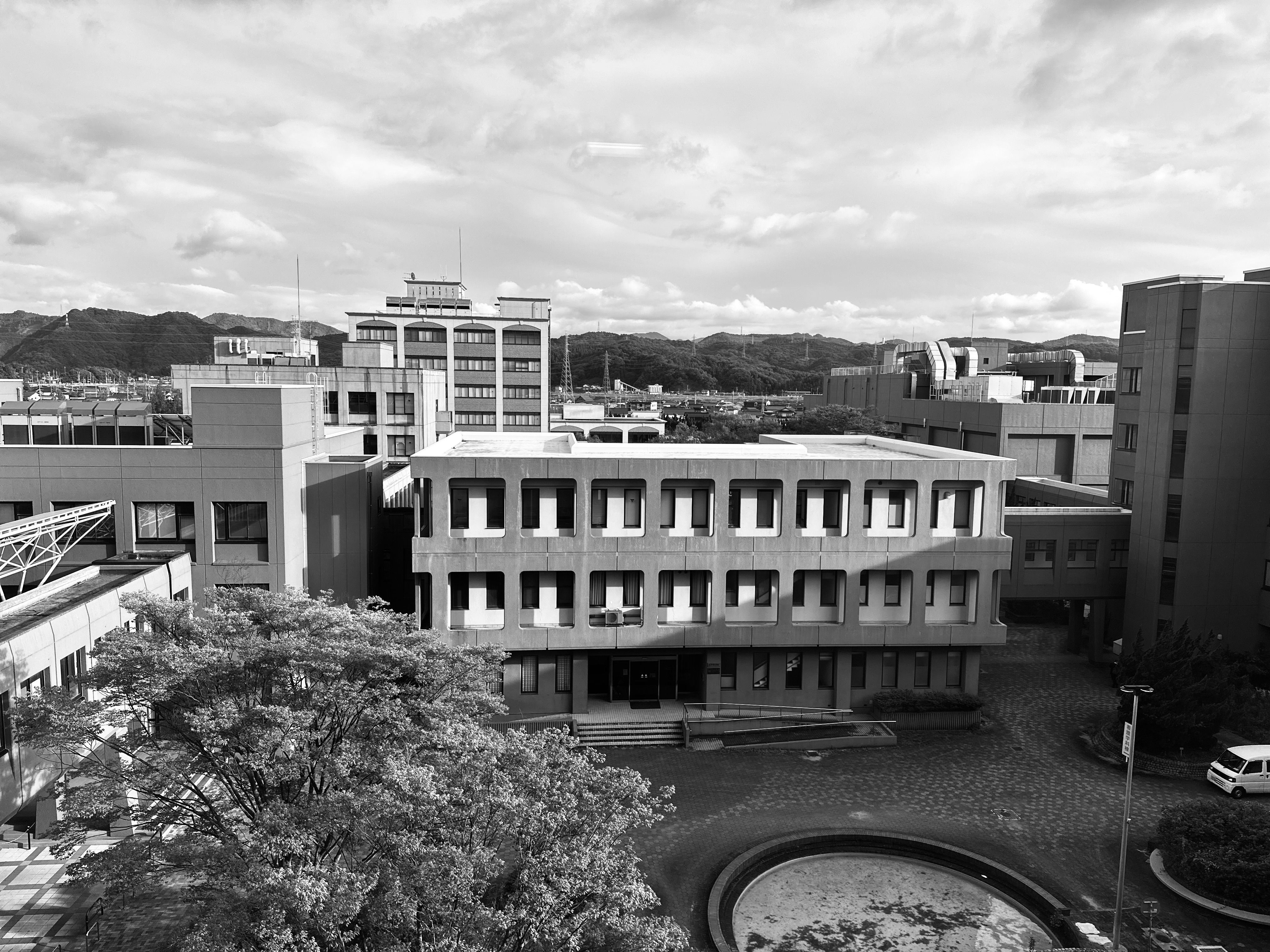 背景に山があるモノクロの現代的な学術ビルの空撮。