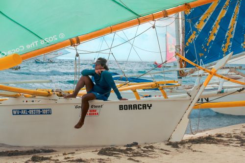 Free A sailor sitting on a traditional paraw sailboat on a sandy beach in Boracay, Philippines. Stock Photo