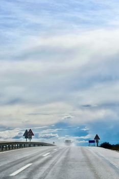 A car drives on an icy highway under a dramatic sky, showcasing winter weather and travel challenges.