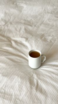 A simple coffee cup rests on a soft, textured bedspread, offering a cozy morning vibe.