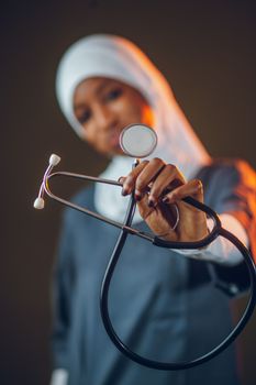 Young nurse wearing a hijab presenting a stethoscope towards the camera.