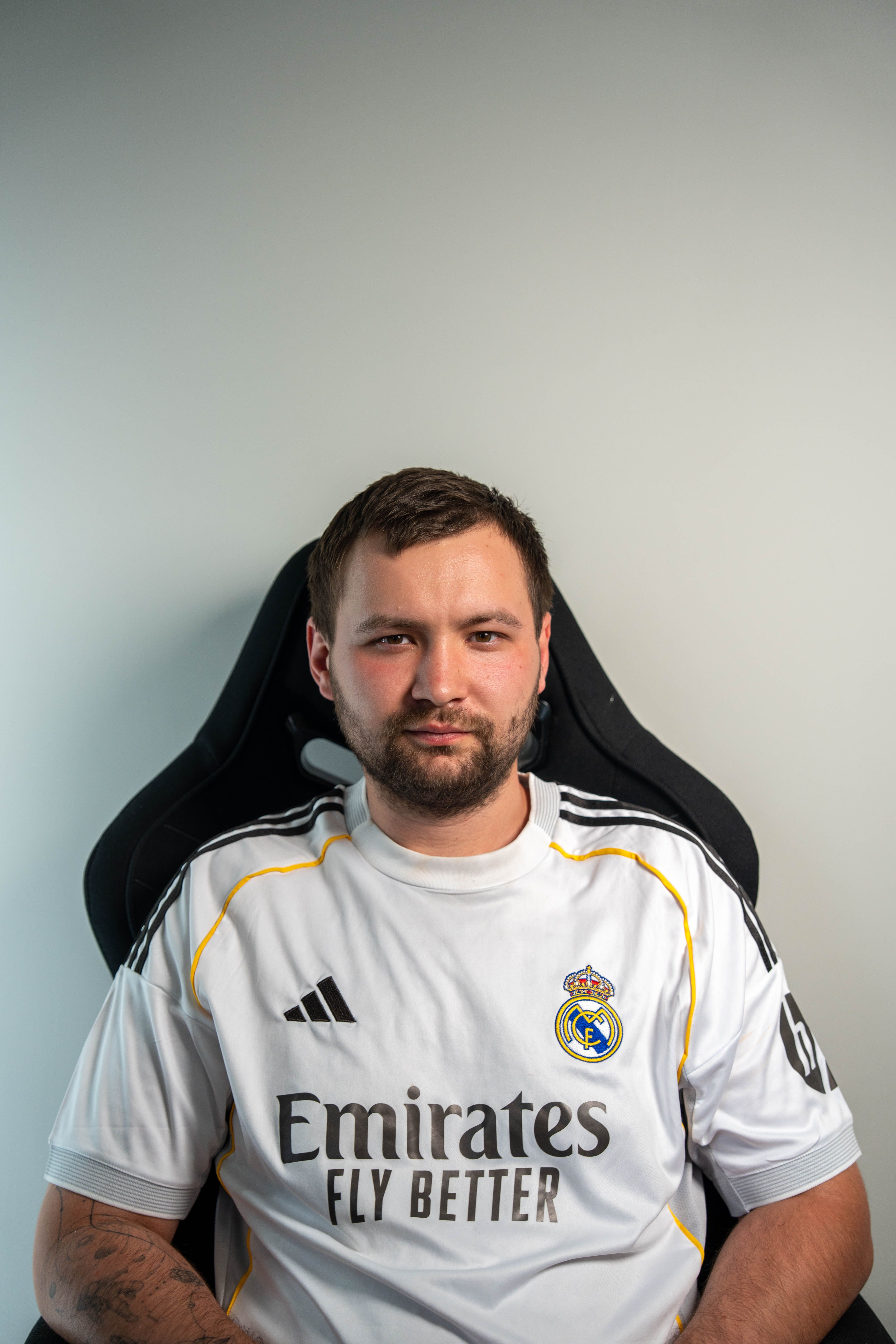 Portrait of a man in a Real Madrid jersey seated indoors, looking directly at the camera.