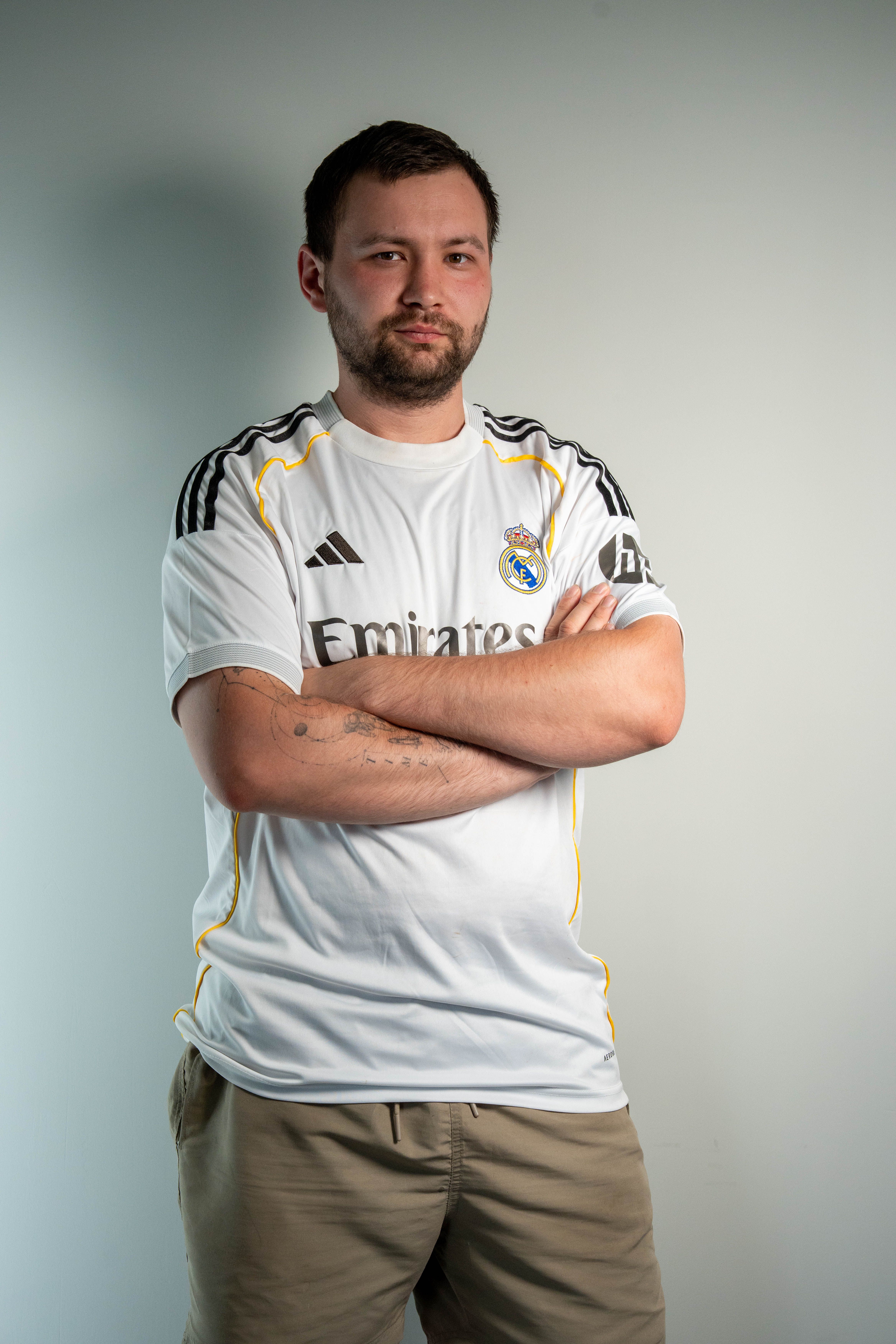 Portrait of a confident man in a Real Madrid jersey crossing his arms indoors.