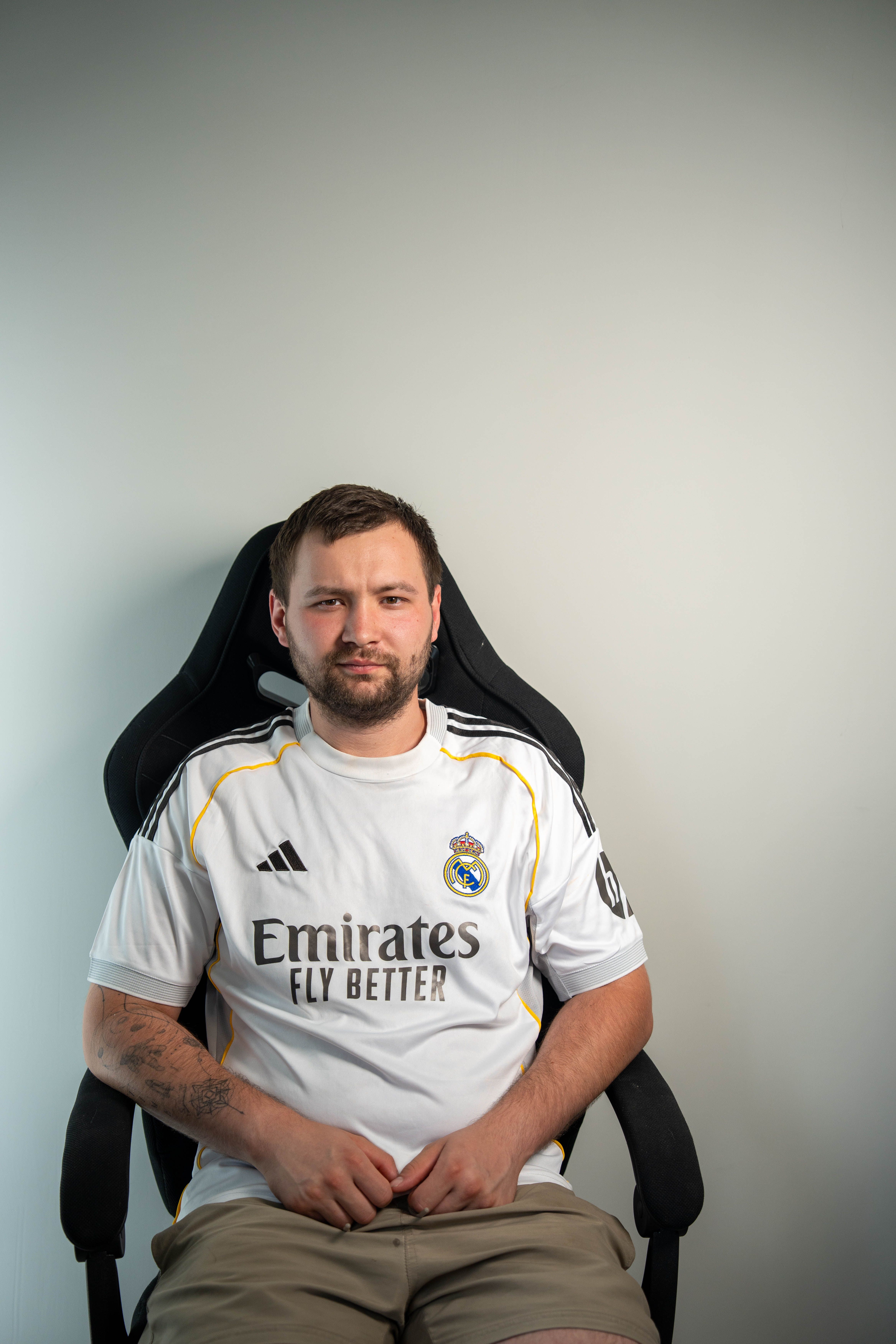 A man wearing a sports jersey sits on a chair, posing casually indoors.
