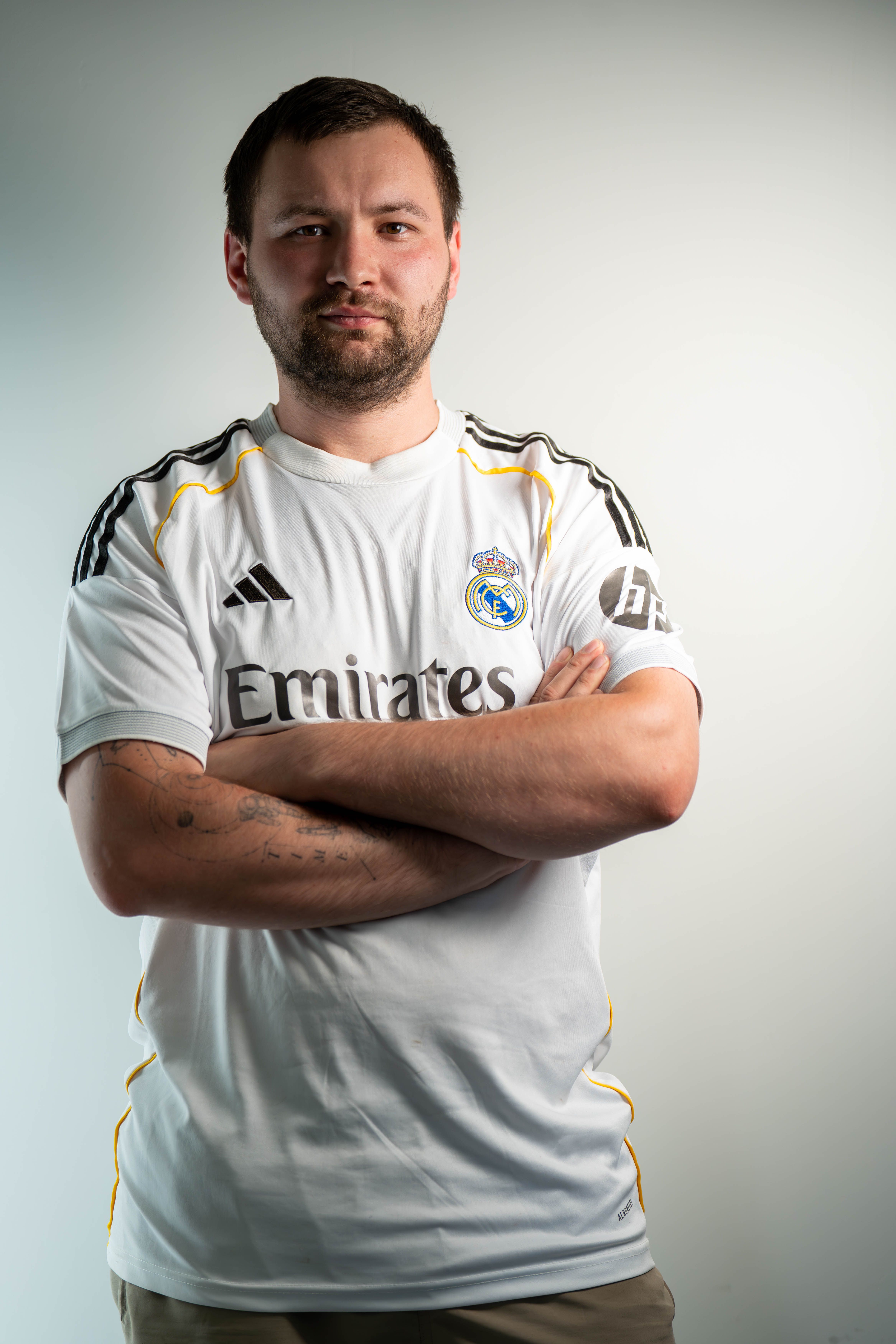 Portrait of a confident man standing with arms crossed wearing a soccer jersey in studio lighting.