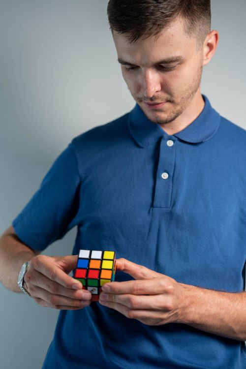 Free Adult man concentrating on solving a Rubik's Cube, dressed casually in blue polo. Stock Photo