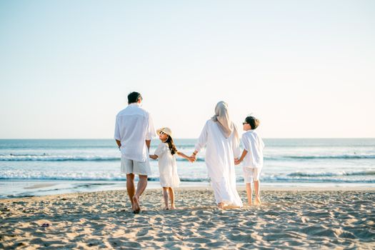A family of four walking hand in hand on a sunny beach, enjoying a bright summer day.