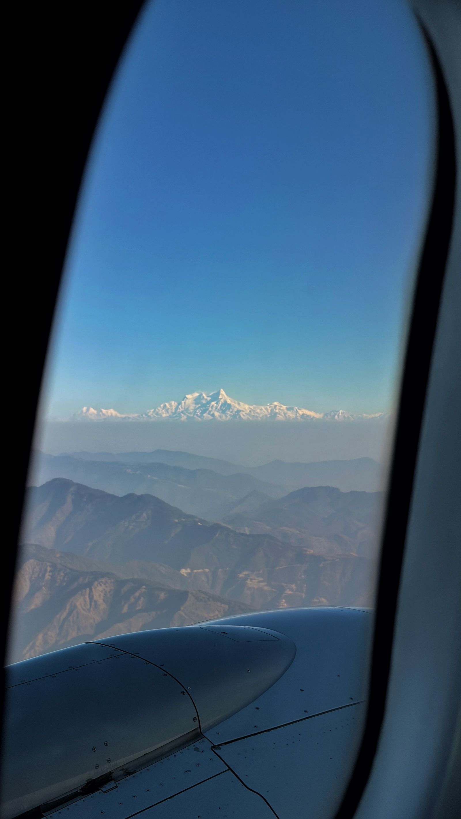 A snow peak of the high Himalaya seen through an airliner window above the brown foothills of Nepal
