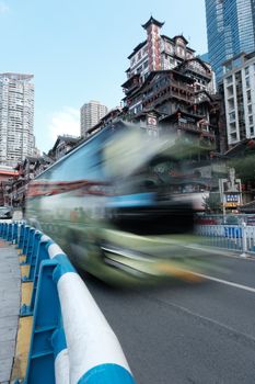 Blurry city bus passes traditional architecture in Chongqing, China.