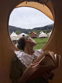 A woman reads inside a tent at a scenic Georgian glamping site with yurts and cabins.